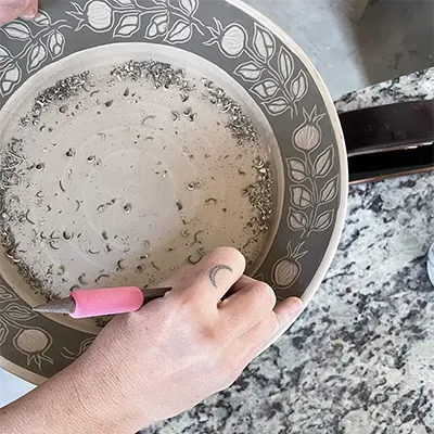 a hand carving pomegranate designs around the edge of a plate