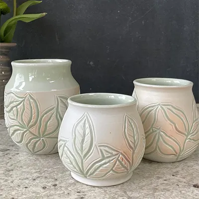 three small white cauldrons wiht subtle red shading, with leaves carved into their surfaces