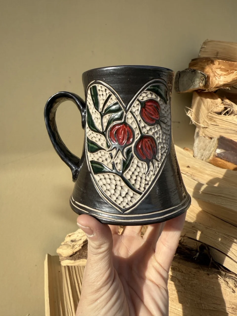 Black mug with carved and painted pomegrantates inside a heart
