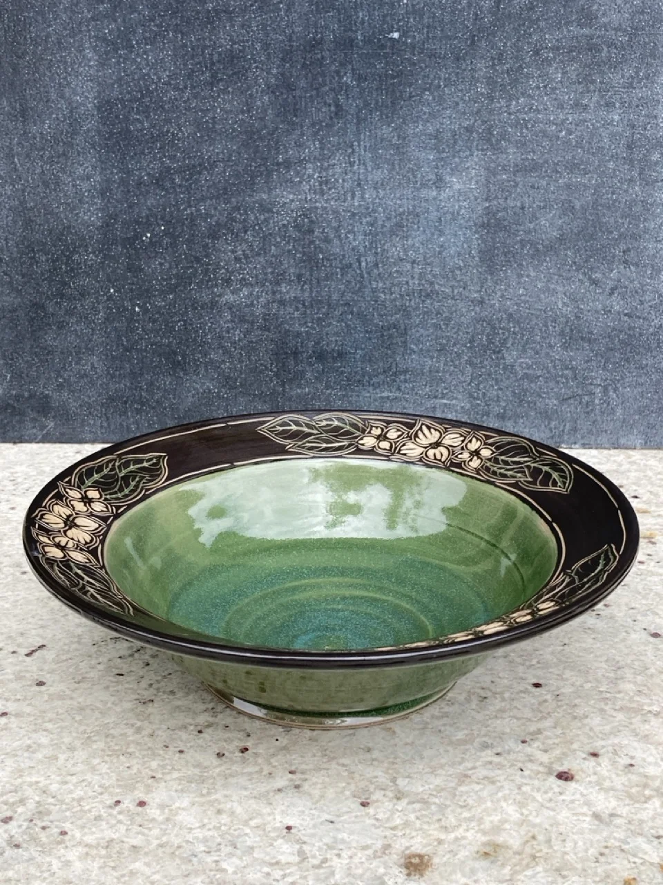 Bowl with carved and painted flowers around a black edge and green interior